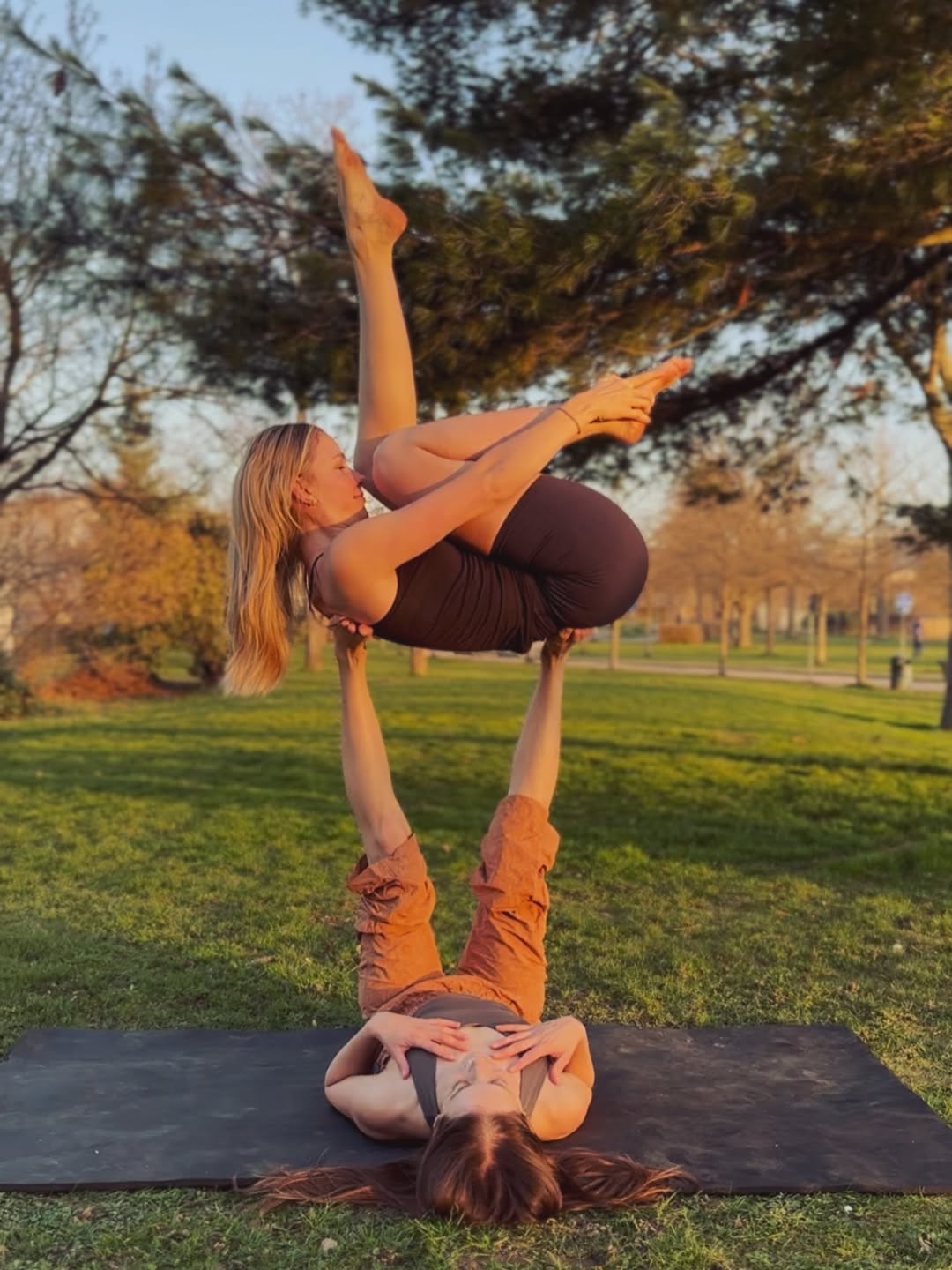 Two practitioners in an AcroYoga flying pose at golden hour